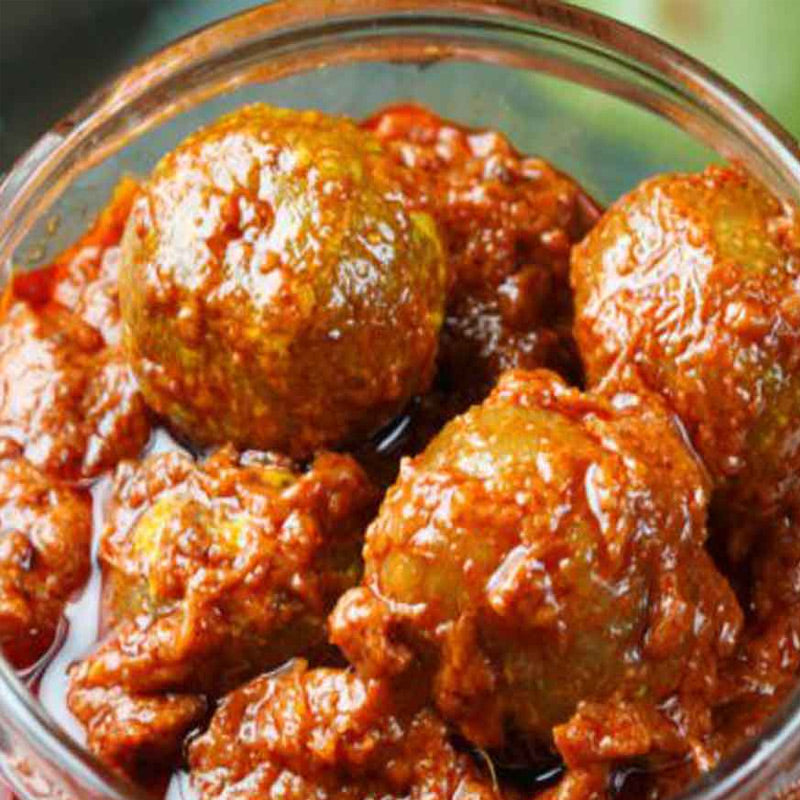 A glass bowl filled with spicy amla pickle, submerged in a red-colored spicy sauce.