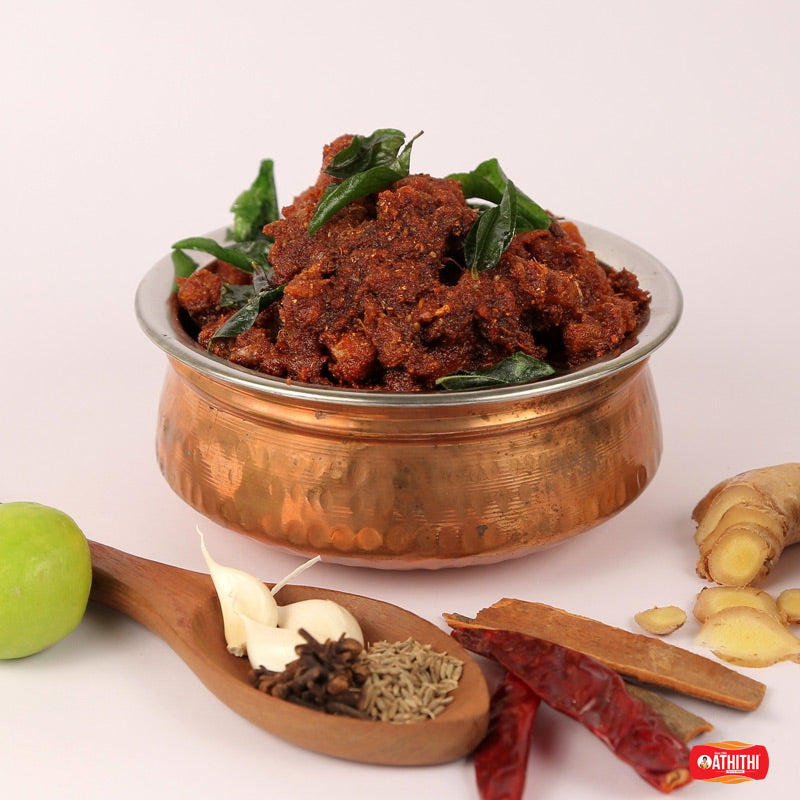 Authentic Andhra style Chicken Pickle served in a traditional copper bowl with fresh curry leaves, handcrafted by Athithi Gruha Foods.