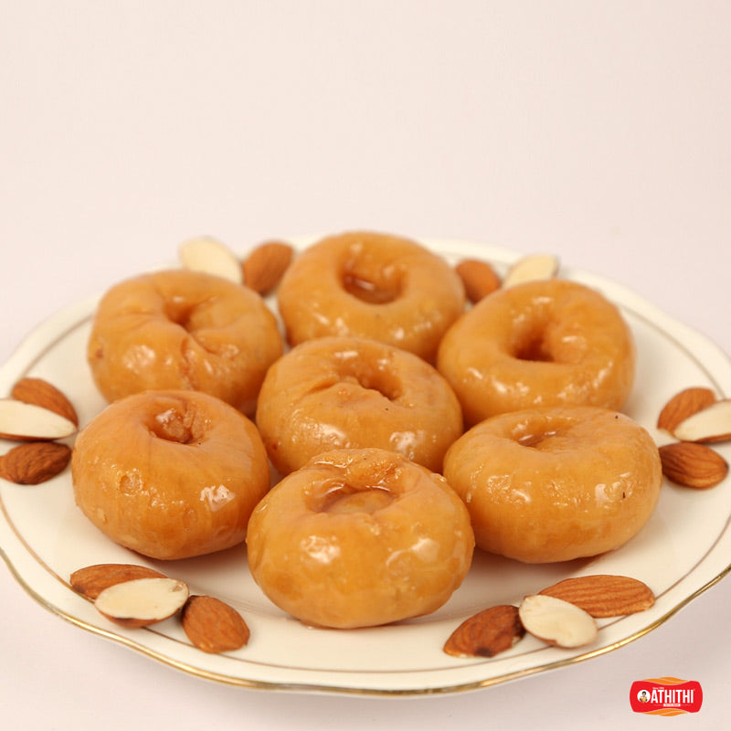 A plate of traditional sweets, specifically donuts, garnished with almonds and cashews.