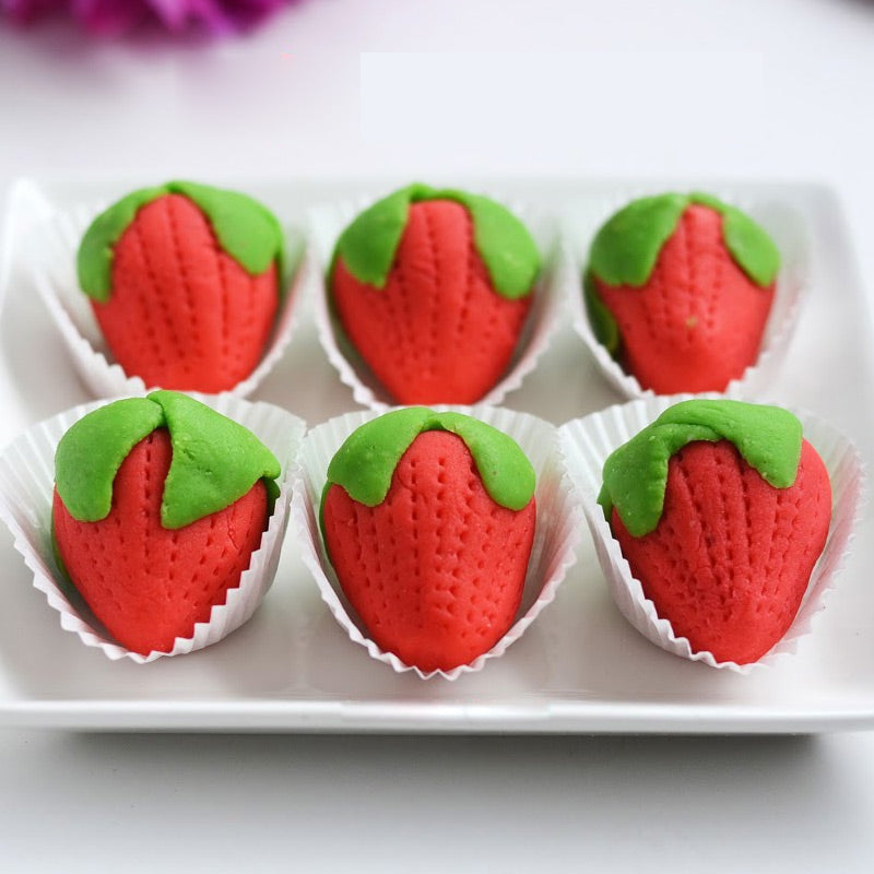Red strawberry-shaped cashew sweets with green leaves in paper cups, handcrafted by Athithi Gruha Foods.