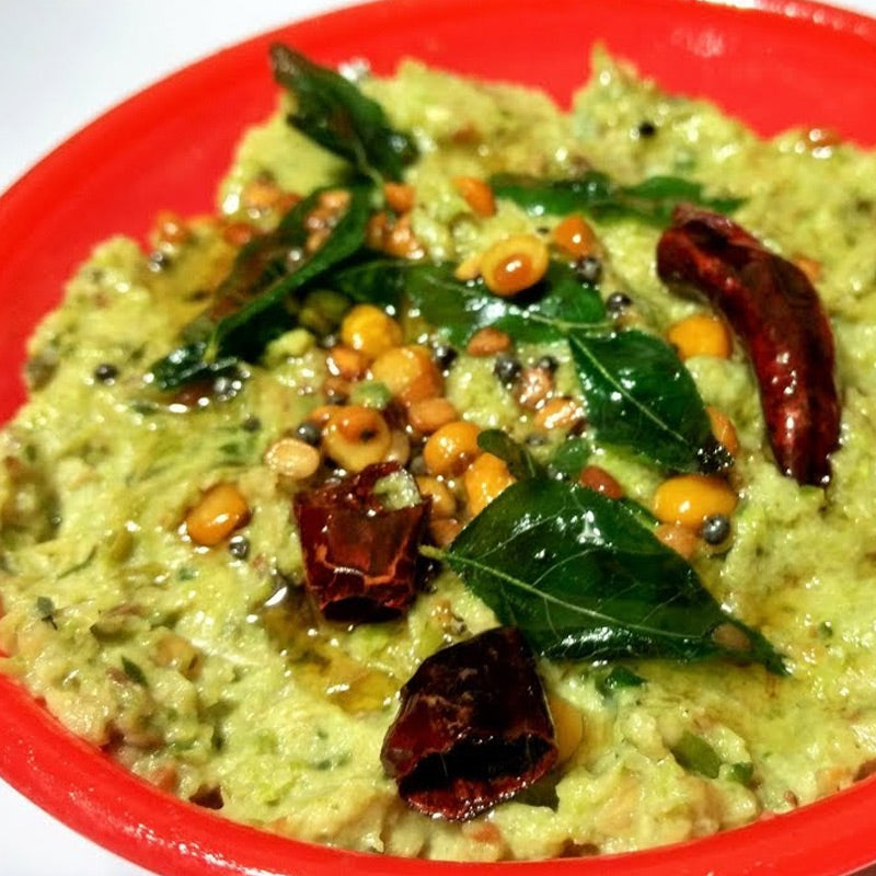A red bowl filled with Dondakaya Roti Pachadi, a spicy Indian pickle, topped with a green leaf and red chili pieces.