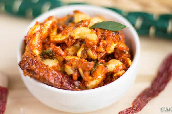 Spicy and tangy Cashew Pickle (Kaju Pickle) in a bowl with curry leaves, handcrafted by Athithi Gruha Foods.
