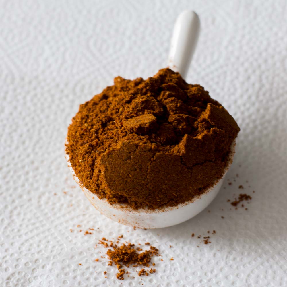 Rich and aromatic Chicken Masala powder served in a white ceramic spoon, handcrafted by Athithi Gruha Foods.